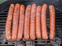 hot dogs and sausages are cooking on the grill