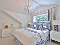 a large bed sitting under a window next to a white dresser and lamp in a bedroom