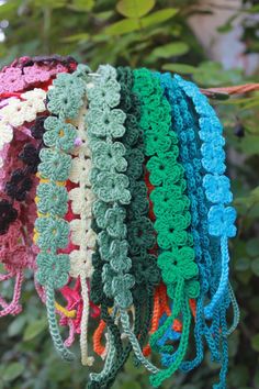 several crocheted headbands hanging from a tree with leaves in the background