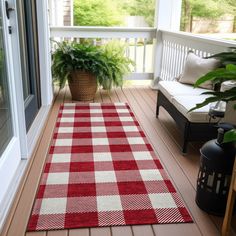 a red and white checkered rug sitting on top of a wooden floor next to a potted plant