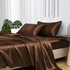 a bed with brown sheets and pillows in a room next to a plant on the floor