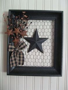 a black and white frame with a star hanging on the wall next to some dried flowers