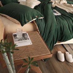 a bed with green sheets and pillows next to a small wooden table on the floor