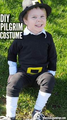 a little boy sitting on the grass wearing a black and white outfit with yellow letters