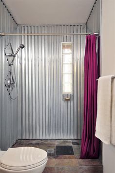 a white toilet sitting next to a shower in a bathroom with pink curtains on the walls