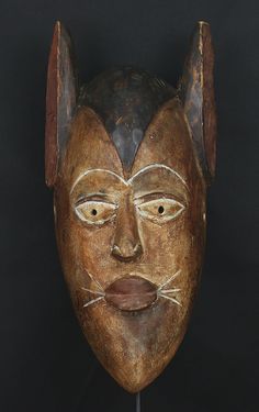 a wooden mask with white lines on it's face and ears, sitting against a black background