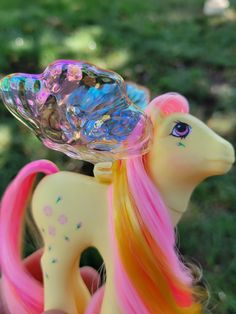 a little pony with pink and yellow hair holding a crystal bowl on its head in the grass