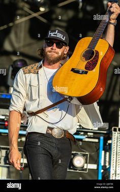 a man holding an acoustic guitar on stage at a music festival, with his hands in the air - stock image