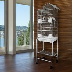 a tall white bird cage sitting on top of a wooden floor next to a window