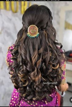 the back of a woman's head with long curly hair and an intricate brooch