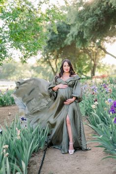 a pregnant woman in a green dress poses for a photo while surrounded by purple flowers