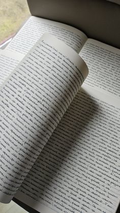 an open book sitting on top of a wooden table next to a window with writing on it