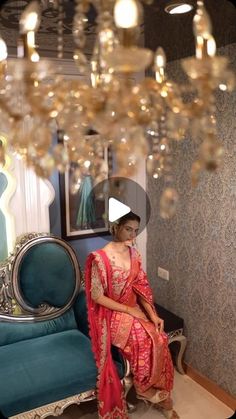 a woman sitting on top of a blue couch in front of a chandelier