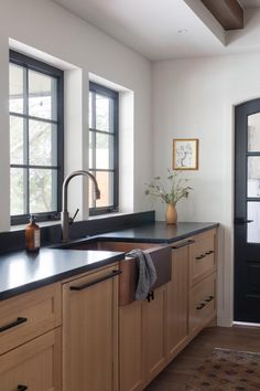 a kitchen with black counter tops and wooden cabinetry, along with two windows that look out onto the outdoors