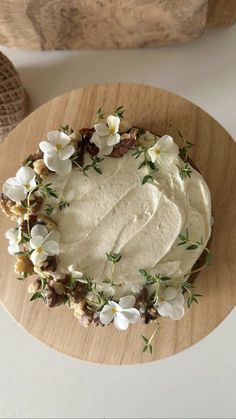 a cake with white frosting and flowers on it sitting on top of a wooden plate