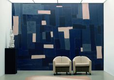 two white chairs sitting in front of a blue and beige wall with squares on it