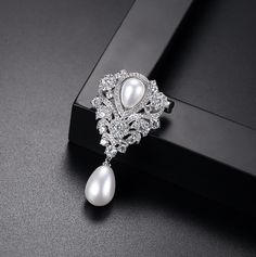 Classic elegance! Iridescent white pearls are paired with clear cubic zirconia that capture the light from every angle with a perfectly translucent appeal. The setting is rhodium plated for a bright finish which enhances the intricate detailing and conveys a modern take on old elegance. Overall length of the brooch is 50mm (approx. 2"). This exquisite design will add a touch of sophistication to any wedding gown or formal ensemble. Vintage Pearl Brooch, Diamond Flower Brooch, Pearl Brooch, Pearl Types, Pin Jewelry, Diamond Flower, Vintage Pearls, Pearl Drop, Flower Brooch