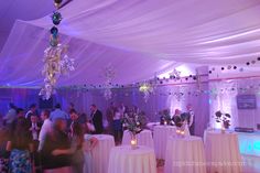 a group of people standing around tables in a room with white drapes on the ceiling