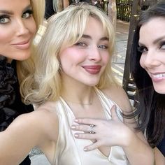 three beautiful women posing for the camera with one holding her hand on her chest and another smiling