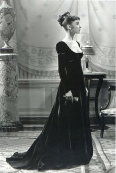 an old black and white photo of a woman in a long dress standing next to a table