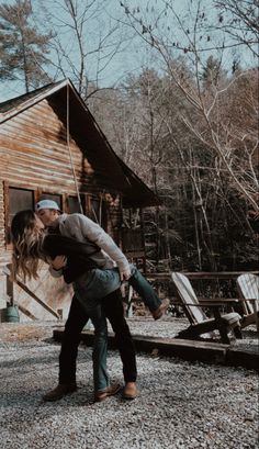 a man and woman kissing in front of a wooden cabin with chairs on the ground