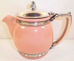 a pink tea pot sitting on top of a white table next to a silver lid