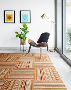 a living room with a chair, rug and potted plant on the floor in front of large windows