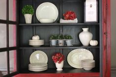 a red china cabinet filled with dishes and vases