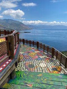 a wooden bench sitting on top of a lush green hillside next to the ocean and mountains