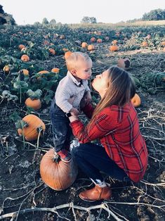 a woman kneeling down next to a baby on top of a pumpkin field