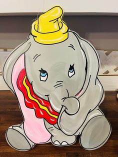 an elephant with a yellow hat on its head sitting on top of a wooden table