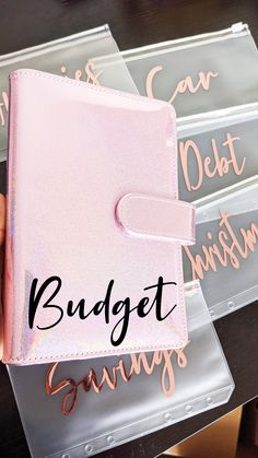 a person holding a pink wallet with the word budget savings written on it and three clear acrylic boxes