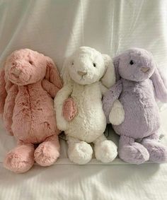 three stuffed animals sitting next to each other on a white sheet covered bed with sheets