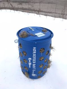 a blue trash can sitting in the snow next to a pole with barbed wire on it