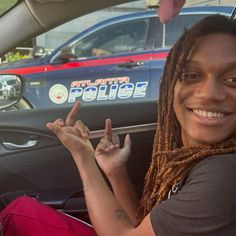 a woman with dreadlocks sitting in a police car and making the peace sign