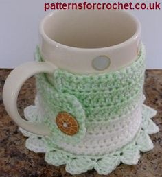 a crocheted coffee cup holder with a button on the front and bottom, sitting on a granite countertop