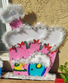 a pink and white decorative object sitting on top of a window sill next to a potted plant