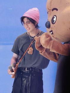 a man standing next to a giant teddy bear holding a fishing rod and wearing a pink hat