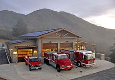 three fire trucks are parked in front of a house with mountains in the back ground