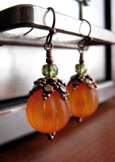 some kind of orange glass beaded earrings hanging from a window sill with green beads