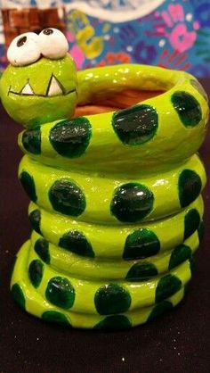 a green and black ceramic snake with polka dots on it's head sitting in a stack of coils