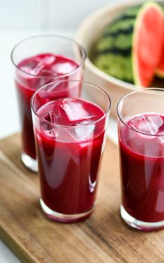 three glasses filled with liquid sitting on top of a wooden tray next to watermelon slices