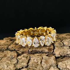 a yellow gold ring with pear shaped diamonds on top of it, sitting on a piece of wood