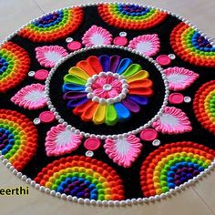 a colorful circular design made with beads on the floor in front of a white wall