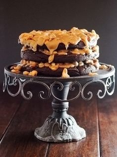 a chocolate cake with caramel drizzled on top sitting on a metal stand