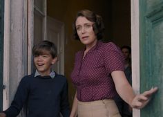 a woman standing next to a boy in front of an open door with his hand out