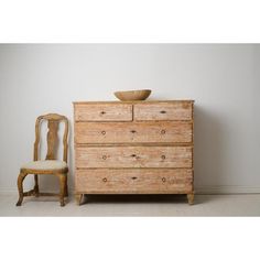 an old wooden dresser with a bowl on top and a chair in front of it