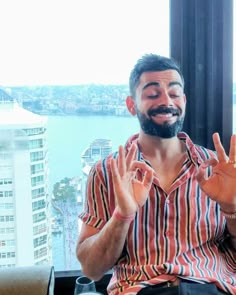 a man sitting in front of a window making the v sign with his hands and smiling