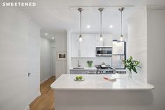 a white kitchen with an island in the middle and three lights hanging from the ceiling