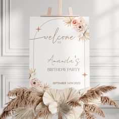 a birthday party sign with flowers and feathers on the front, hanging from a wooden easel